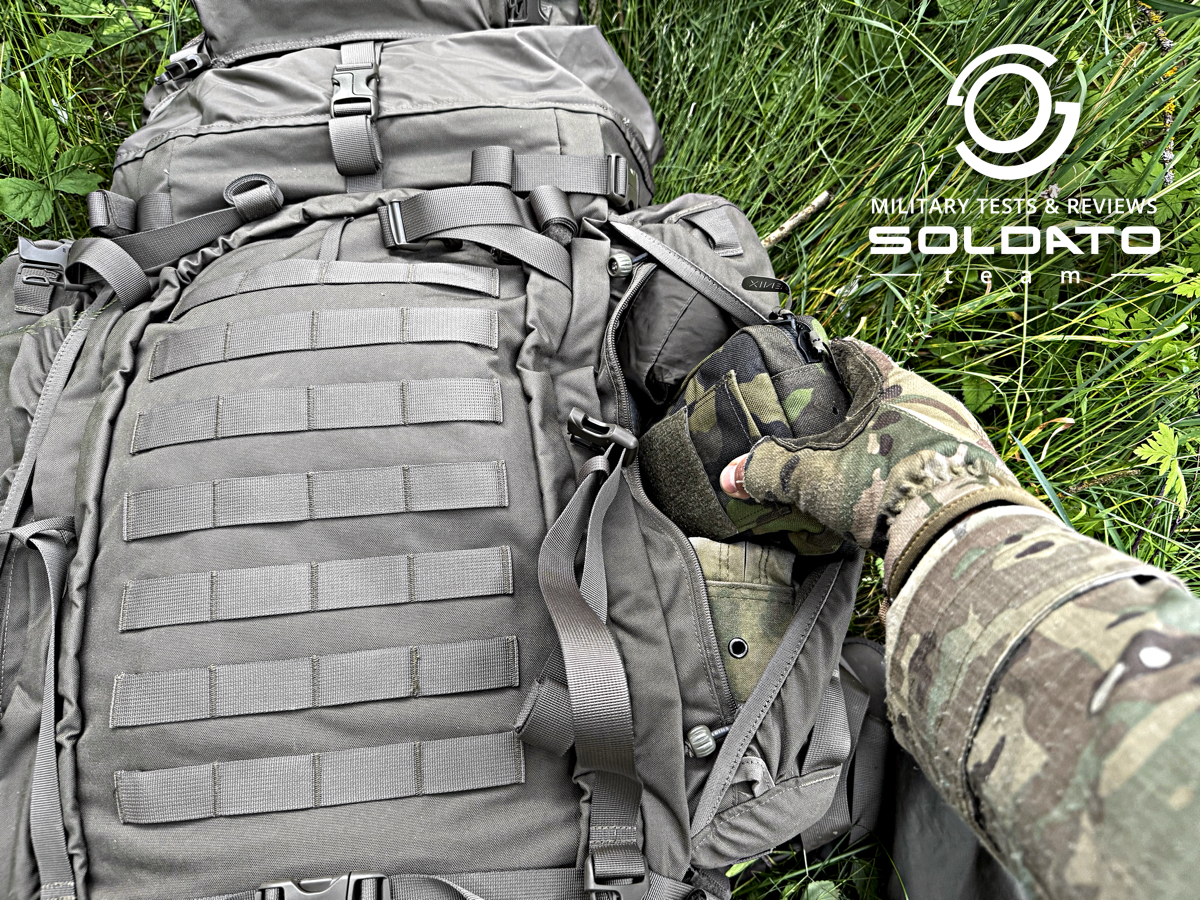 Vyjmutí vybavení z boční kapsy s netradičním zavíráním batohu Snigel 100l.  